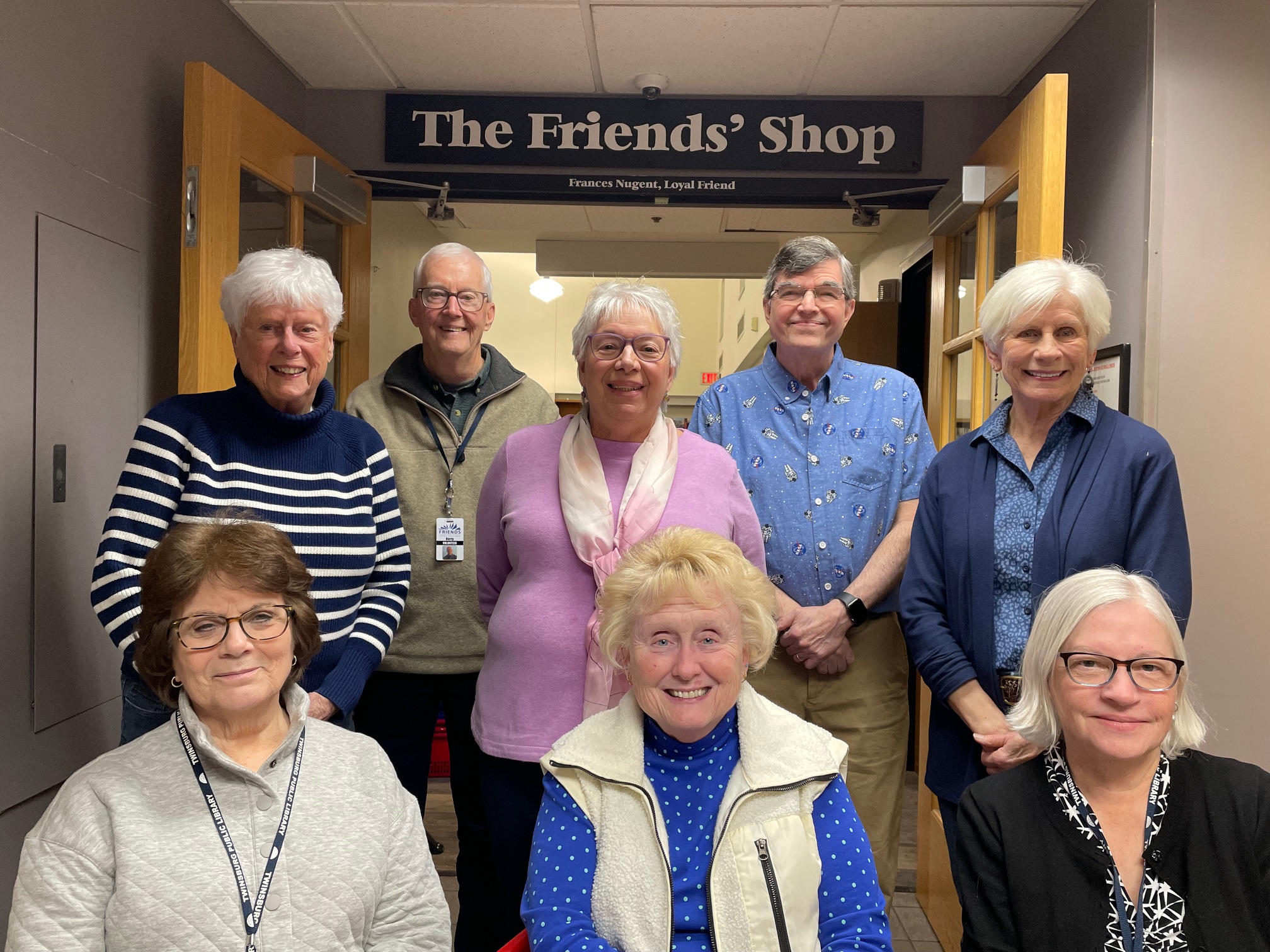 Eight Friends of the Library Board members pose in front of The Friends' Shop